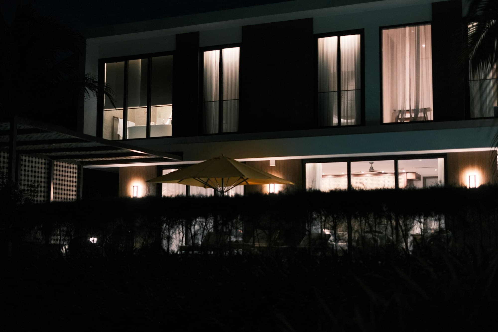 A modern house at night, its rooms lit behind tall windows